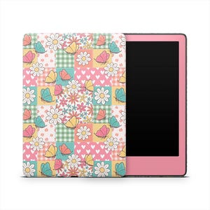 May include: A pink e-reader with a colorful cover featuring a patchwork design. The cover displays butterflies, daisies, and hearts in shades of pink, yellow, blue, and green. The e-reader's screen is black.