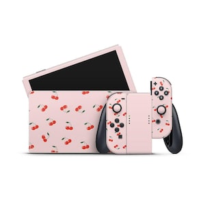 Op de afbeelding: Een roze Nintendo Switch-console en controllers met een kersenpatroon. De Switch is open en toont een zwart scherm. De controllers zijn zwart en roze met zwarte knoppen. De hoes heeft ook het kersenpatroon.