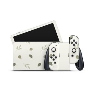 Peut inclure: Une console de jeu blanche avec un étui et des manettes assortis. La console et les manettes présentent un motif de feuilles dans des tons de vert et de gris. Les manettes ont des accents et des boutons noirs.