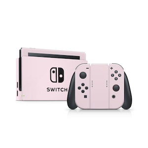 May include: A light pink Nintendo Switch console and controllers. The console has the word "SWITCH" printed on it, along with the Nintendo logo. The controllers are light pink with black accents and buttons.