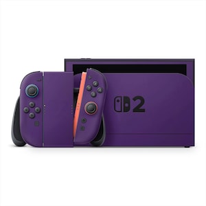 May include: A purple video game console with detachable controllers. The controllers are purple with black buttons and a blue joystick. The console has the number "2" printed on it in black. The screen is black.
