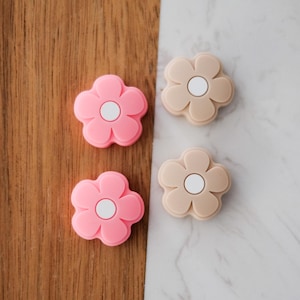 Può includere: Quattro tiretti per cassetti in silicone a forma di fiore, due rosa e due beige, con un cerchio centrale bianco.
