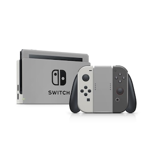 Puede incluir: Una consola Nintendo Switch gris con un juego de mandos Joy-Con a juego. La consola tiene la palabra "SWITCH" impresa en la parte delantera. Los mandos son blancos, grises y negros.