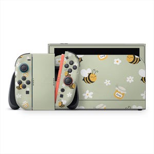Könnte beinhalten: Eine Nintendo Switch-Konsole und Controller mit einem hellgrünen Bienen- und Blumenmuster. Die Controller haben schwarze Knöpfe und eine rote Seite. Die Konsole hat ein passendes Design mit einem Honigglas.