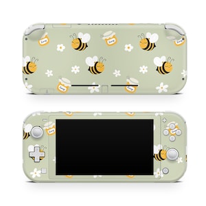 Könnte beinhalten: Eine grüne Nintendo Switch Lite Konsole mit einer benutzerdefinierten Haut, die ein Muster aus Bienen, Honiggläsern und weißen Blumen zeigt. Die Konsole wird von vorne und hinten gezeigt.