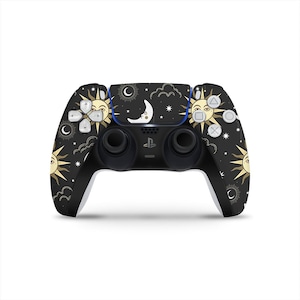 Könnte beinhalten: Schwarzer PlayStation 5-Controller mit einem Himmelsdesign mit Sonnen, Monden und Sternen. Der Controller hat eine schwarze Basis mit goldenen und weißen Akzenten. Die Tasten und das Steuerkreuz sind sichtbar.