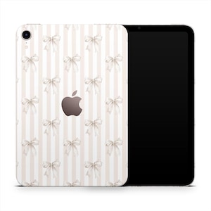 May include: An iPad with a decorative case featuring a pattern of white bows on a striped background of beige and white. The Apple logo is visible on the back of the device. The screen is black.