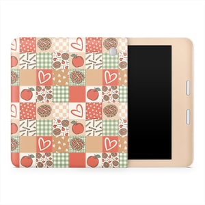 Pode incluir: Uma capa para tablet com um design de patchwork com ilustrações de maçãs, corações e tortas em tons de vermelho, verde e bege. A capa está presa a um tablet dourado com tela preta.