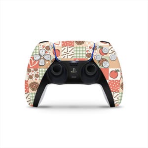 Peut inclure: Une manette PlayStation 5 noire et blanche avec un motif patchwork représentant des pommes, des tartes et des cœurs. La manette a un accent bleu et la disposition standard des boutons.
