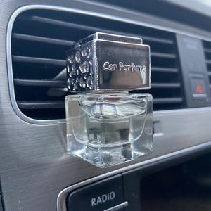 May include: A silver car air freshener with a clear glass bottle and the text "Car Perfume" on the top.
