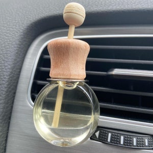 May include: A wooden car air freshener with a clear glass bottle and a wooden stick. The bottle is filled with a light yellow liquid.