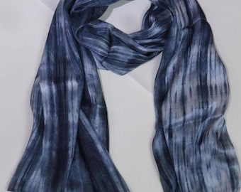 Op de afbeelding: Een blauwe en witte gestreepte zijden sjaal met een subtiel tie-dye effect. De sjaal is dubbelgevouwen en gedrapeerd over een wit oppervlak. De tekst "Handy Silk" is zichtbaar in de rechterbenedenhoek van de afbeelding.