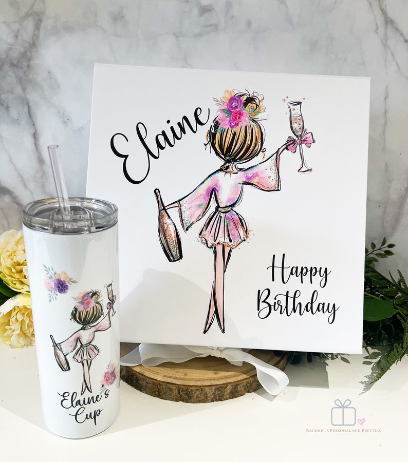 K&ouml;nnte beinhalten: Ein wei&szlig;er Becher mit einem Strohhalm und einem rosa-violetten Blumendesign. Der Becher zeigt ein Cartoon-Bild einer Frau im Bademantel, die ein Glas Champagner h&auml;lt. Der Text "Elaine's Cup" ist auf den Becher gedruckt. Eine wei&szlig;e Box mit einem rosa-violetten Blumendesign und dem Text "Elaine Happy Birthday" befindet sich im Hintergrund.