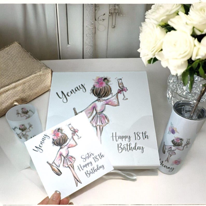 K&ouml;nnte beinhalten: Eine wei&szlig;e Geschenkbox mit einem personalisierten Design, das eine Frau in einem rosa Morgenmantel zeigt, die ein Glas Champagner h&auml;lt. Die Box enth&auml;lt eine Karte mit dem Text "Schwester Gl&uuml;cklicher 18. Geburtstag" und einen Becher mit einem &auml;hnlichen Design. Die Box ist mit dem Namen "Yenay" und dem Text "Gl&uuml;cklicher 18. Geburtstag" verziert.