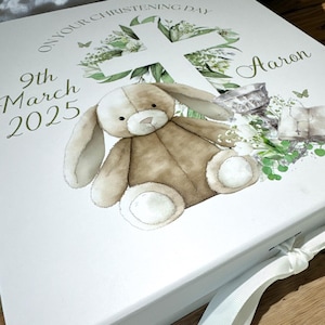 May include: White keepsake box with a green floral design, a cross, a bunny rabbit, and the text "On your christening day 9th March 2025 Aaron".