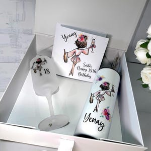 K&ouml;nnte beinhalten: Eine wei&szlig;e Geschenkbox mit einem wei&szlig;en Band. In der Box befindet sich eine wei&szlig;e Karte mit einer Zeichnung einer Frau, die ein Glas Champagner h&auml;lt. Die Karte sagt "Yenay Sister Happy 18th Birthday". Au&szlig;erdem gibt es ein wei&szlig;es Weinglas und einen wei&szlig;en Becher mit der gleichen Zeichnung und dem Namen "Yenay".