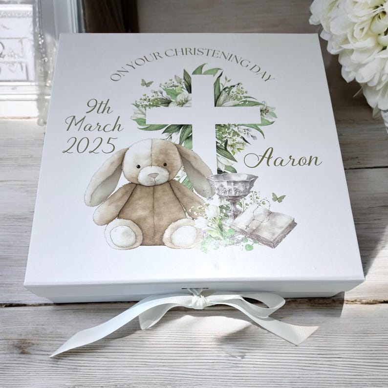 May include: White gift box with a light brown bunny, a cross, and flowers. The box has the text "On your christening day 9th March 2025 Aaron".