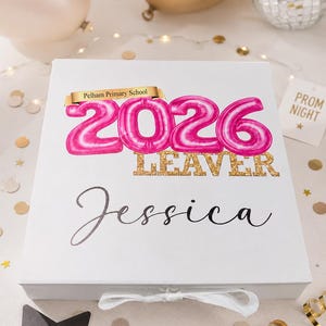 May include: A white rectangular keepsake box with a white ribbon closure. The lid features a gold banner reading Pelham Primary School, pink balloon-style numbers 2026, the word LEAVER in gold glitter, and the name Jessica in black script.