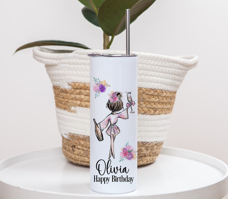 K&ouml;nnte beinhalten: Ein wei&szlig;er Edelstahlbecher mit einem rosa und violetten Blumendesign und einer Cartoon-Illustration einer Frau, die eine Flasche Champagner und ein Glas h&auml;lt. Der Becher ist mit dem Namen "Olivia" und dem Text "Happy Birthday" bedruckt.
