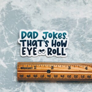 May include: A white sticker with blue and green text that reads "DAD Jokes. THAT'S HOW EYE ROLL" with two cartoon eyes in the middle of the text.