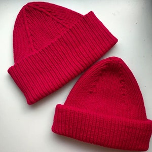May include: Two bright red knitted beanies. The beanies are made of a thick, textured yarn and have a simple, classic design.