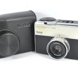 Peut inclure: Un appareil photo Kodak Instamatic 233 vintage avec un corps noir et argenté, et un étui en cuir noir. L'appareil photo porte l'inscription "Instamatic 233 Camera" et "Kodak". L'objectif est marqué "Kodak Reomar".