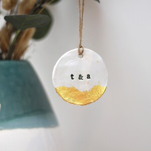 May include: White ceramic ornament with gold accents and the text "t & a" in black lettering.