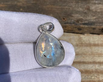 May include: A teardrop-shaped moonstone pendant with a silver bail. The moonstone is iridescent and has a milky white color.