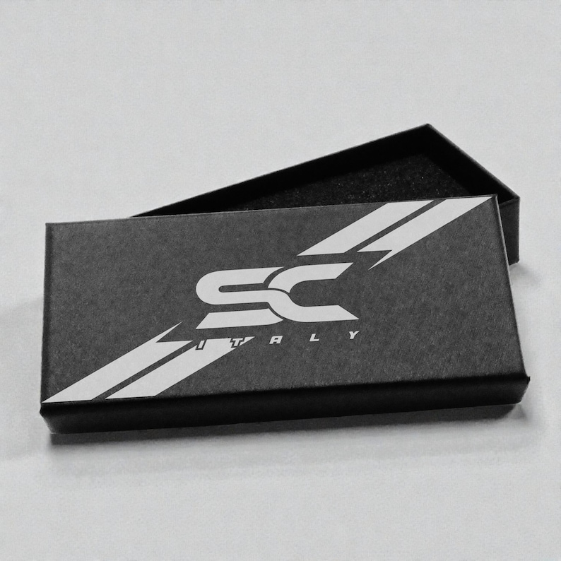 May include: Black rectangular box with the letters "SC" in white, and the word "TOTALLY" underneath. The box is open, revealing a black interior. White diagonal stripes accent the top of the box.