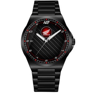 Op de afbeelding: Zwarte polshorloge met een koolstofvezel wijzerplaat en rode accenten. Het horloge heeft een Honda-logo in het midden en een zwarte metalen band. De wijzerplaat toont de cijfers 1 tot en met 12.