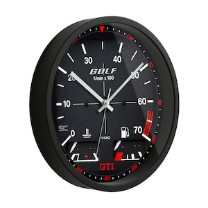 May include: Black wall clock with a gauge face design. The clock face features the word "GOLF" and "GTI" in red, along with white hands and numbers. The clock has a black frame and a red accent around the edge.