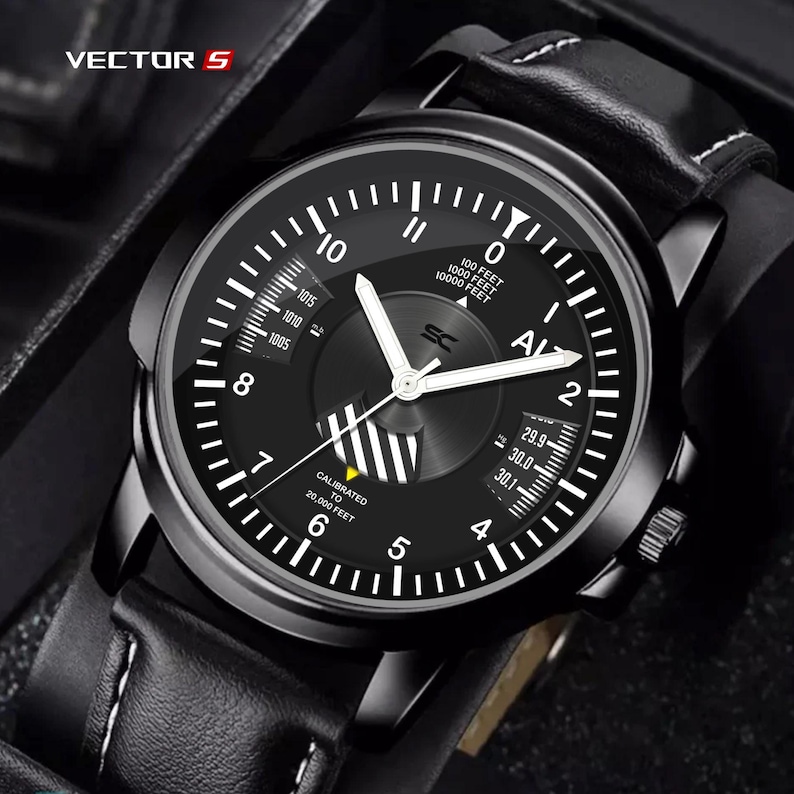 May include: Black analog watch with white hands and numerals. The watch face displays the text "VECTOR S" and "AL". The watch has a black leather band with white stitching.