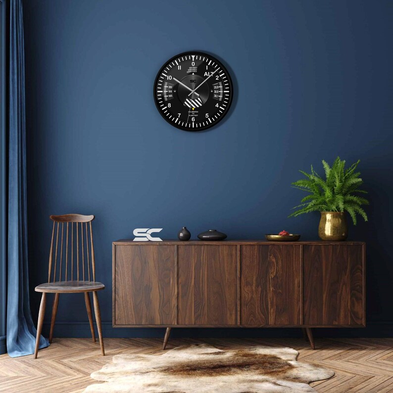 May include: A black wall clock with white markings and hands, mounted on a dark blue wall. The clock has a unique design with multiple scales and the word "ALT" visible. The clock is part of a room decor.