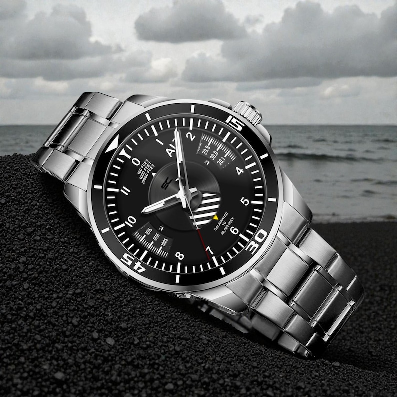 May include: A stainless steel wristwatch with a black dial and a silver band. The watch face features white numerals, a rotating bezel, and a second hand. The watch is displayed on a dark surface with a cloudy sky and ocean in the background.