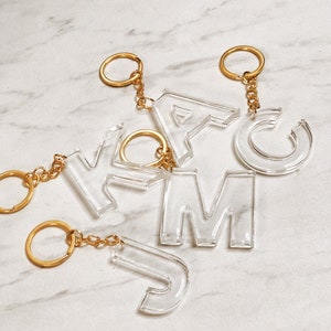 May include: A set of six clear acrylic letter keychains with gold metal rings and chains. The letters are J, M, C, Y, A, and F.