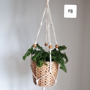 May include: A white macrame plant hanger with wooden beads, holding a woven basket with a green plant. The hanger is labeled "F8".