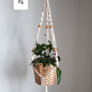 May include: A white macrame plant hanger with wooden beads, holding a woven basket with a green plant. The hanger is labeled "F6".