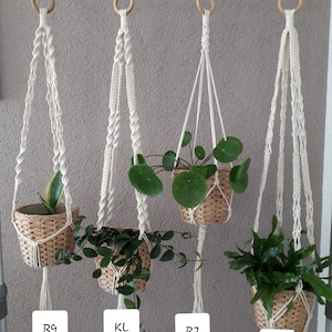 Könnte beinhalten: Vier Makramee-Pflanzenhänger mit Holzringen und Quasten, die an einer Metallstange hängen. Jeder Hänger hat eine andere Pflanze in einem geflochtenen Korb. Die Hänger sind mit R9, KL, R7 und R3 beschriftet.