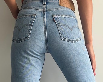 May include: A pair of light blue denim jeans with a straight leg fit. The jeans have a high waist and a classic five-pocket design. The jeans are worn with brown suede ankle boots.
