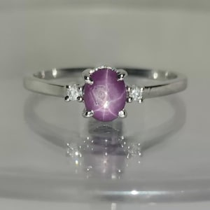May include: A silver ring with a purple star sapphire gemstone and two smaller diamonds on the band.