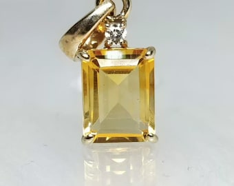 May include: A gold pendant featuring a rectangular, yellow gemstone with a small, clear accent stone. The pendant has a simple, elegant design, with a loop for a chain.