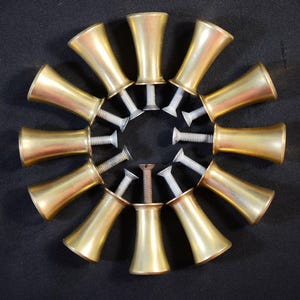 May include: A circular arrangement of brass-coloured cabinet knobs, each with a silver screw. The knobs have a flared, trumpet-like shape. The arrangement is set against a dark, textured background.