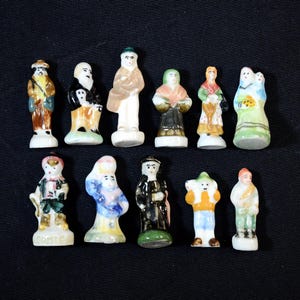 Puede incluir: Una colección de pequeñas figuras de cerámica pintadas a mano que representan varias figuras con trajes tradicionales. Las figuras son de varios colores, incluyendo marrón, blanco, negro, verde y azul. Dispuestas sobre una superficie negra.