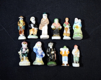 Puede incluir: Una colección de pequeñas figuras de cerámica pintadas a mano que representan varias figuras con trajes tradicionales. Las figuras son de varios colores, incluyendo marrón, blanco, negro, verde y azul. Dispuestas sobre una superficie negra.