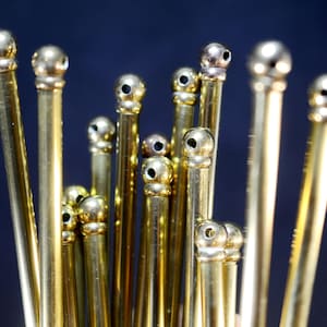 Pode incluir: Um close-up de um grupo de hastes metálicas douradas com pontas arredondadas. As hastes estão dispostas em um aglomerado, com algumas das pontas sobrepostas.