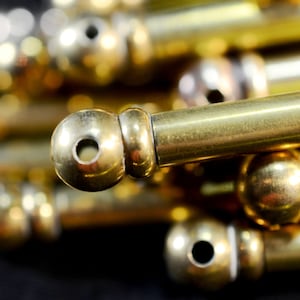 May include: Close-up of a pile of gold-colored metal curtain rods with round finials. The rods are smooth and shiny.