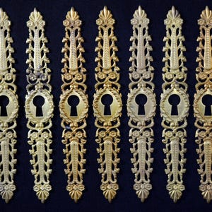Puede incluir: Ocho escudos de cerradura de metal dorado adornados con intrincados diseños florales. Cada escudo tiene una cerradura en el centro.