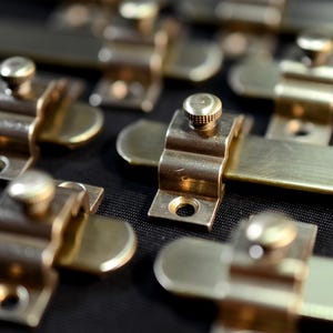 May include: Close-up of several brass door bolt locks with a textured finish. The bolts are arranged in a row on a black surface.