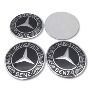 Op de afbeelding: Vier cirkelvormige Mercedes-Benz embleem badges. Elke badge heeft een zwarte achtergrond met een zilveren ster embleem en de woorden "MERCEDES" en "BENZ" in zilver. Er is ook een zilveren cirkel aanwezig.
