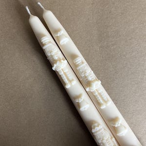 Puede incluir: Dos velas de color marfil con diseños en relieve de un cascanueces y una campana. Las velas miden aproximadamente 25 cm de largo.